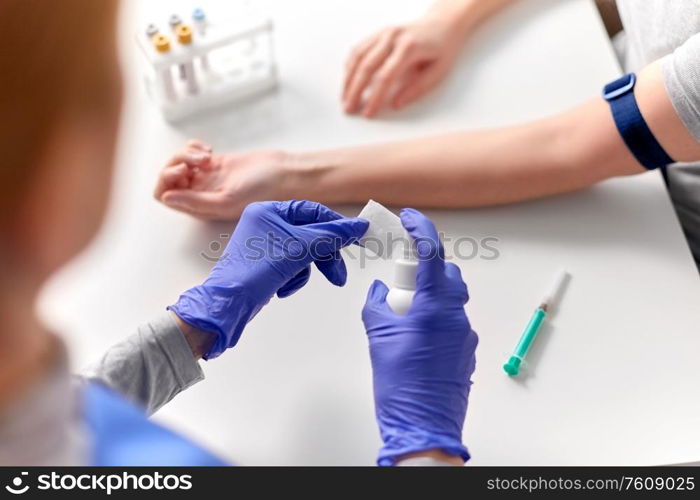 medicine, healthcare and diabetes concept - close up of doctor in gloves with sanitizer disinfecting wipe before taking blood from patient&rsquo;s hand for test at hospital. doctor and patient preparing for blood test