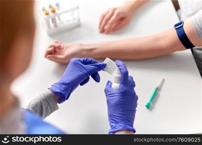 medicine, healthcare and diabetes concept - close up of doctor in gloves with sanitizer disinfecting wipe before taking blood from patient&rsquo;s hand for test at hospital. doctor and patient preparing for blood test