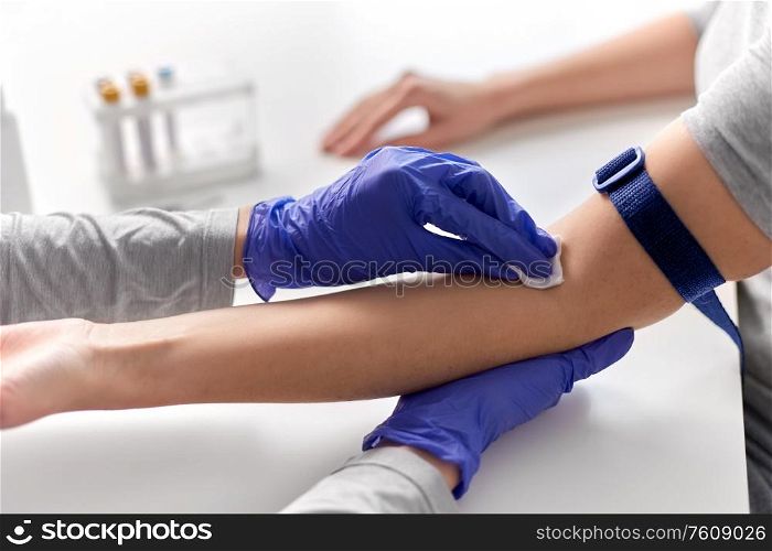 medicine, healthcare and diabetes concept - close up of doctor in gloves disinfecting patient&rsquo;s hand with wipe before taking blood for test at hospital. doctor and patient preparing for blood test