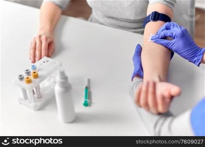 medicine, healthcare and diabetes concept - close up of doctor in gloves disinfecting patient&rsquo;s hand with wipe before taking blood for test at hospital. doctor and patient preparing for blood test