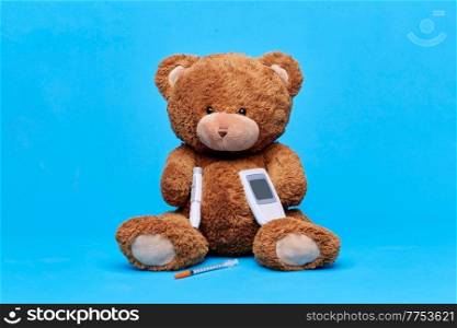 medicine, healthcare and diabetes concept - teddy bear toy with syringe, glucometer and insulin pen device over blue background. teddy bear with glucometer and insulin syringe