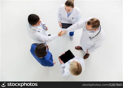 medicine, healthcare and gesture concept - group of doctors with tablet pc computers greeting by handshake at hospital. doctors with tablet pc doing handshake at hospital