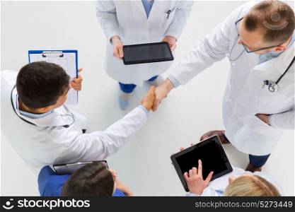 medicine, healthcare and gesture concept - group of doctors with tablet pc computers greeting by handshake at hospital. doctors with tablet pc doing handshake at hospital