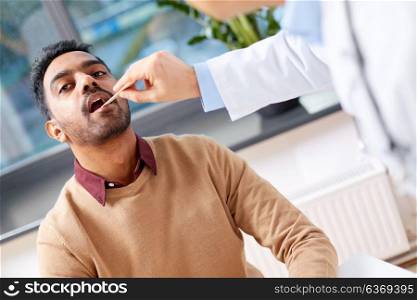 medicine, healthcare and laryngology concept - doctor or laryngologist with tongue depressor examining male patient throat at clinic. doctor examining patient throat at clinic