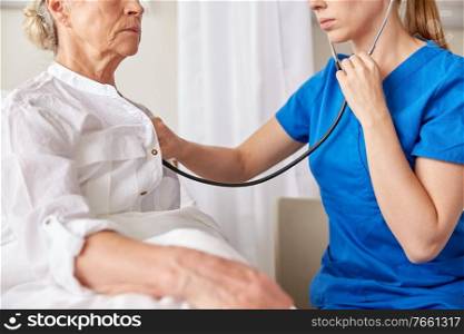medicine, healthcare and old age concept - female doctor or nurse with stethoscope checking heartbeat or breath of senior woman at hospital. doctor with stethoscope and old woman at hospital