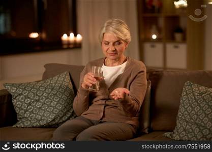 medicine, healthcare and old age concept - senior woman with pills and glass of water at home at night. senior woman with water and medicine at home