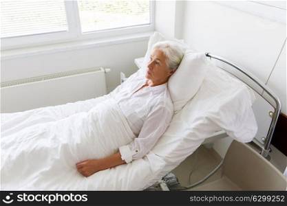 medicine, healthcare and old people concept - sad senior woman lying on bed at hospital ward. sad senior woman lying on bed at hospital ward
