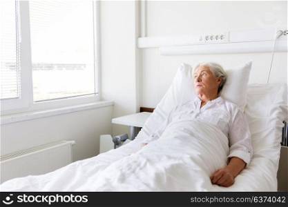 medicine, healthcare and old people concept - sad senior woman lying on bed at hospital ward. sad senior woman lying on bed at hospital ward