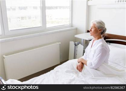 medicine, healthcare and old people concept - sad senior woman sitting on bed at hospital ward. sad senior woman sitting on bed at hospital ward
