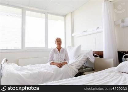 medicine, healthcare and old people concept - sad senior woman sitting on bed at hospital ward. sad senior woman sitting on bed at hospital ward