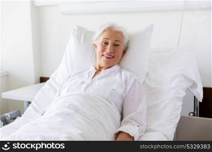 medicine, healthcare and old people concept - smiling senior woman lying on bed at hospital ward. smiling senior woman lying on bed at hospital ward