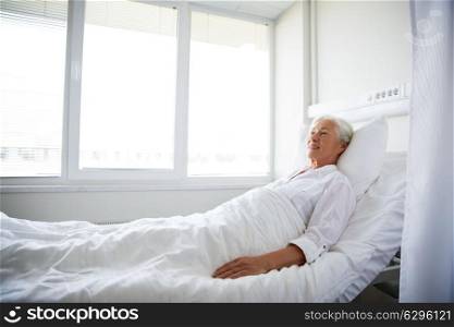 medicine, healthcare and old people concept - smiling senior woman lying on bed at hospital ward. smiling senior woman lying on bed at hospital ward