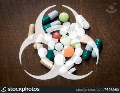 medicine, healthcare and pandemic concept - biohazard caution sign over pills on wooden table. biohazard caution sign over medicines on table