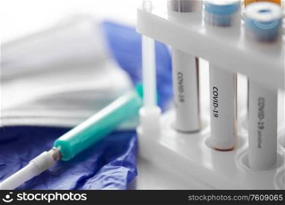 medicine, healthcare and pandemic concept - close up of beakers with coronavirus blood test in holder, syringe and glove at laboratory. beakers with coronavirus blood test in holder
