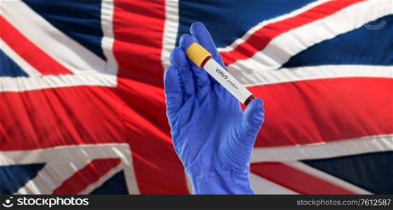 medicine, healthcare and pandemic concept - close up of hand in protective medical glove holding beaker with positive virus blood test over flag of united kingdom. hand holding beaker with positive virus blood test