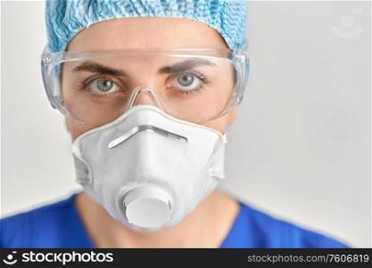 medicine, healthcare and pandemic concept - close up of young female doctor or nurse wearing goggles and face protective mask or respirator for protection from virus disease. doctor in goggles and protective face mask