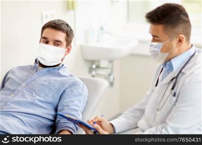 medicine, healthcare and pandemic concept - doctor wearing face protective medical mask for protection from virus disease with clipboard and young male patient at medical exam at hospital. male doctor and patient in masks at hospital