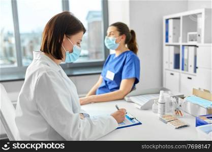 medicine, healthcare and pandemic concept - female doctor in medical protective mask with clipboard and nurse or medical worker at hospital. doctor with clipboard and nurse at hospital