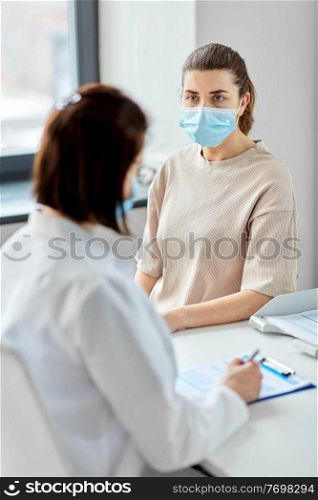 medicine, healthcare and pandemic concept - female doctor in medical protective mask or nurse with clipboard and patient at hospital. doctor with clipboard and patient at hospital