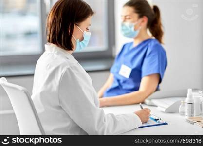 medicine, healthcare and pandemic concept - female doctor in medical protective mask with clipboard and nurse or medical worker at hospital. doctor with clipboard and nurse at hospital