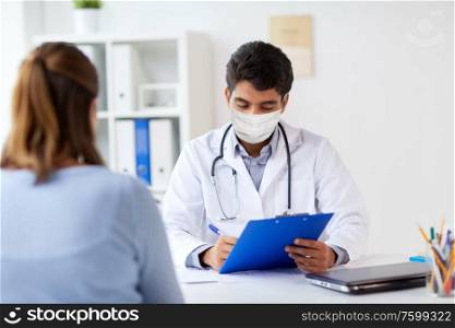 medicine, healthcare and pandemic concept - indian doctor wearing protective medical mask for protection from virus with clipboard and patient at hospital. doctor in medical mask and patient at hospital