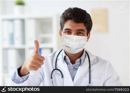 medicine, healthcare and pandemic concept - indian male doctor with stethoscope wearing protective medical mask for protection from virus showing thumbs up at clinic. doctor in medical mask at clinic showing thumbs up