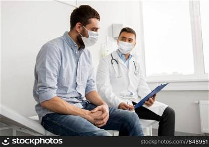 medicine, healthcare and pandemic concept - male doctor wearing face protective medical mask for protection from virus disease with clipboard and young man patient meeting at hospital. male doctor and patient in masks at hospital