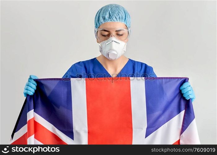 medicine, healthcare and pandemic concept - young female doctor or nurse wearing goggles and face protective mask or respirator for protection from virus disease holding flag of england. doctor in goggles and mask holding flag of england