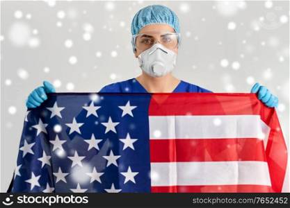 medicine, healthcare and pandemic concept - young female doctor or nurse wearing goggles and face protective mask or respirator holding flag of america in winter over snow. doctor in goggles and mask holding flag of america