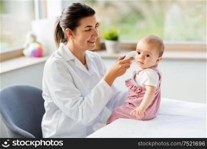 medicine, healthcare and pediatrics concept - female pediatrician doctor with digital infrared thermometer measuring baby girl patient&rsquo;s ear temperature at clinic or hospital. doctor with thermometer measures baby temperature