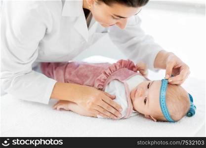 medicine, healthcare and pediatrics concept - female pediatrician doctor with measure tape measuring baby girl patient&rsquo;s head at clinic or hospital. pediatrician doctor measuring bab&rsquo;s head at clinic