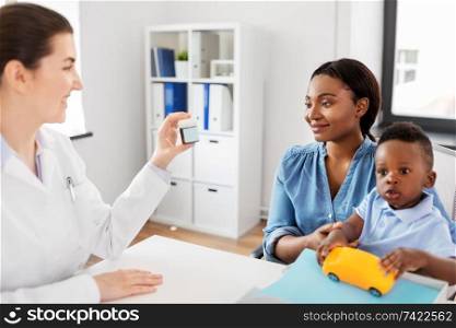 medicine, healthcare and pediatry concept - caucasian doctor giving medication to african american mother with baby son at clinic. doctor giving medicine to woman with son at clinic