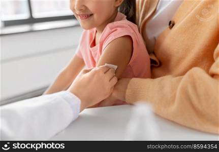 medicine, healthcare and pediatry concept - close up of doctor or pediatrician disinfecting arm skin of little girl patient with mother at clinic. doctor preparing child for vaccination at clinic