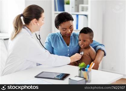 medicine, healthcare and pediatry concept - doctor with stethoscope listening to african american baby boy on medical exam at clinic. doctor with stethoscope listening baby at clinic