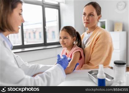 medicine, healthcare and pediatry concept - female doctor or pediatrician with syringe making vaccine injection to little girl patient at clinic. mother vaccinating her little daughter at clinic
