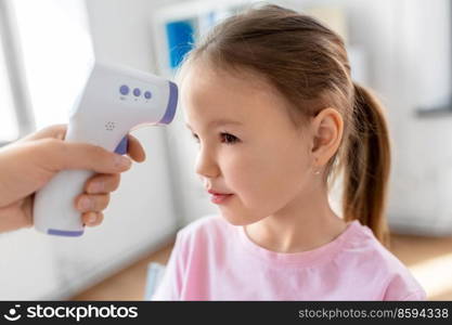medicine, healthcare and pediatry concept - female doctor’s or pediatrician’s hand measuring little girl patient’s temperature with infrared forehead thermometer at clinic. doctor measuring girl’s temperature at hospital