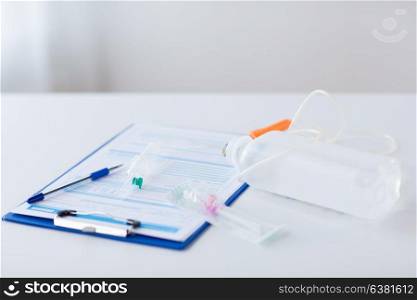 medicine, healthcare and people concept - close up of clipboard with medical report, drop counter and catheter on table. close up of medical report and drop counter