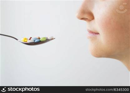 medicine, healthcare and people concept - close up of female face and spoon with pills. close up of female face and spoon with pills