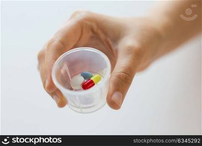 medicine, healthcare and people concept - close up of female hand holding cup with pills. close up of female hand with pills in medicine cup