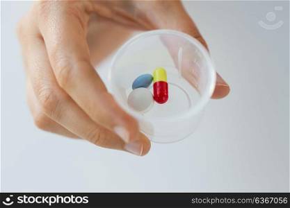 medicine, healthcare and people concept - close up of female hand holding cup with pills. close up of female hand with pills in medicine cup