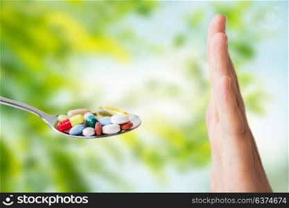 medicine, healthcare and people concept - close up of female hand refusing from pills on spoon over green natural background. hand of woman refusing from pills on spoon