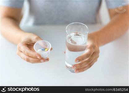 medicine, healthcare and people concept - close up of female hands holding cup with pills and glass of water. close up of hands with pills and glass of water