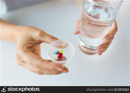 medicine, healthcare and people concept - close up of female hands holding cup with pills and glass of water. close up of hands with pills and glass of water