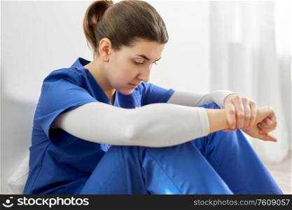 medicine, healthcare and people concept - close up of sad young female doctor or nurse sitting on floor at hospital. sad doctor or nurse sitting on floor at hospital
