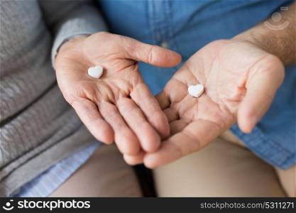 medicine, healthcare and people concept - close up of senior couple hands with heart shaped pills. close up of couple hands with heart shaped pill