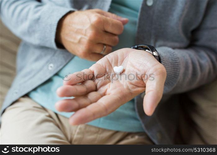 medicine, healthcare and people concept - close up of senior man hand with heart shaped pill. close up of senior man hand with heart shaped pill