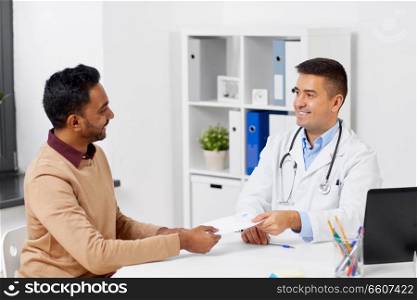 medicine, healthcare and people concept - doctor giving prescription to male patient at clinic. doctor and male patient meeting at clinic