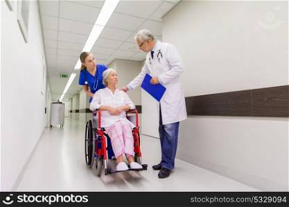 medicine, healthcare and people concept - doctor, nurse and senior woman patient in wheelchair at hospital corridor. medics and senior patient in wheelchair at clinic