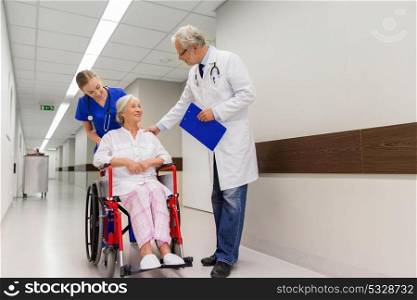 medicine, healthcare and people concept - doctor, nurse and smiling senior woman patient in wheelchair at hospital corridor. medics and senior patient in wheelchair at clinic