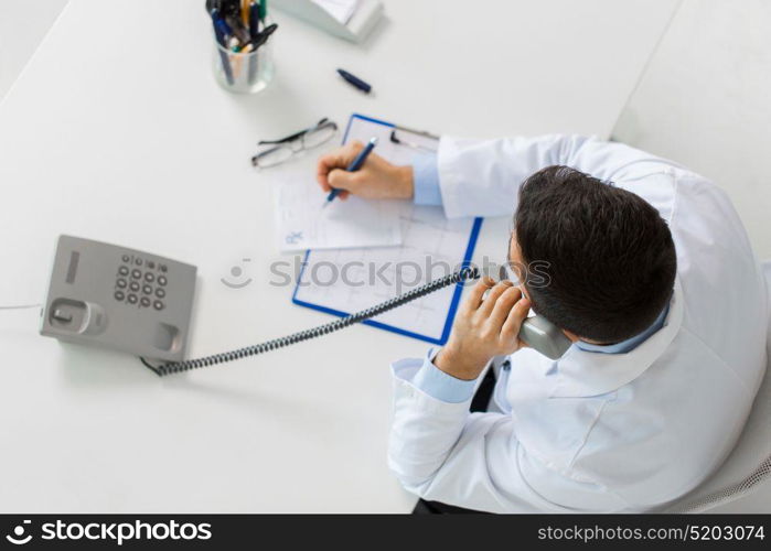 medicine, healthcare and people concept - doctor with cardiogram and prescription calling on phone at table in clinic. doctor with prescription calling on phone